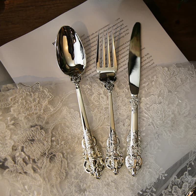 Talheres de luxo banhados a prata com detalhes ornamentados sobre um tecido floral branco