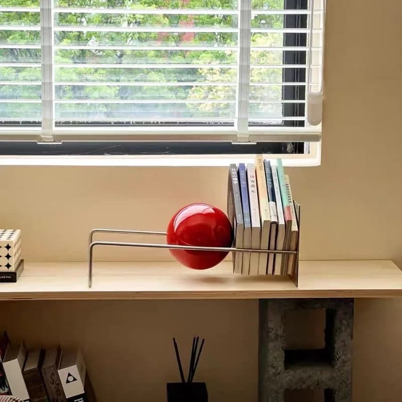 Estante de livros de mesa moderna em aço inoxidável prata com esfera vermelha em ambiente iluminado