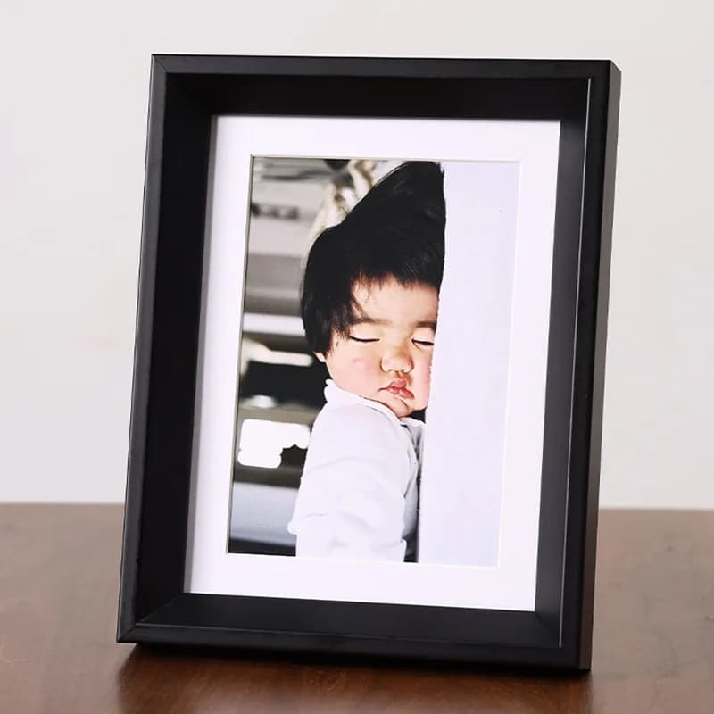 Porta-retrato minimalista preto com moldura branca exibindo foto de bebê dormindo