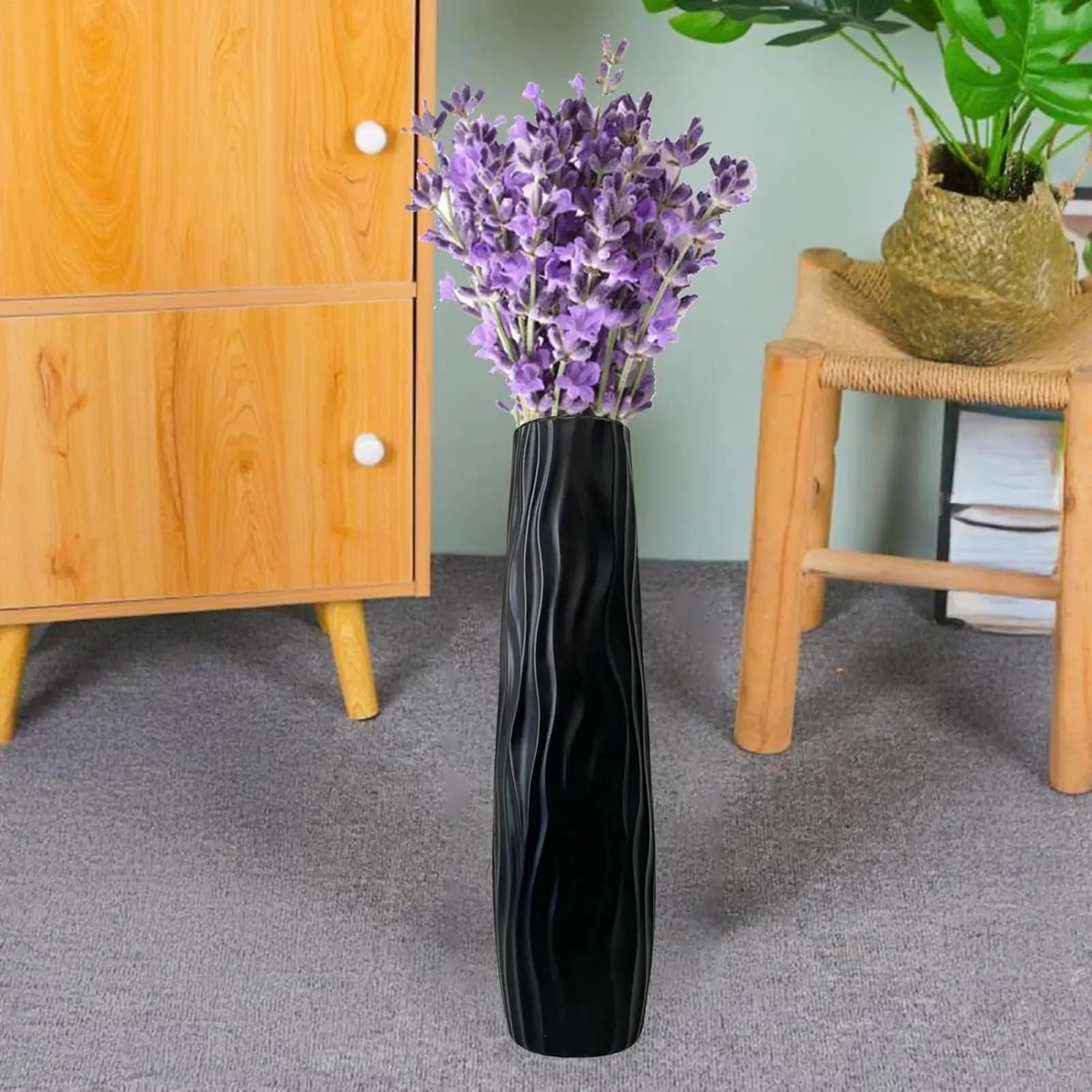 Vaso de chão grande preto com textura ondas preenchido com flores roxas em ambiente interno
