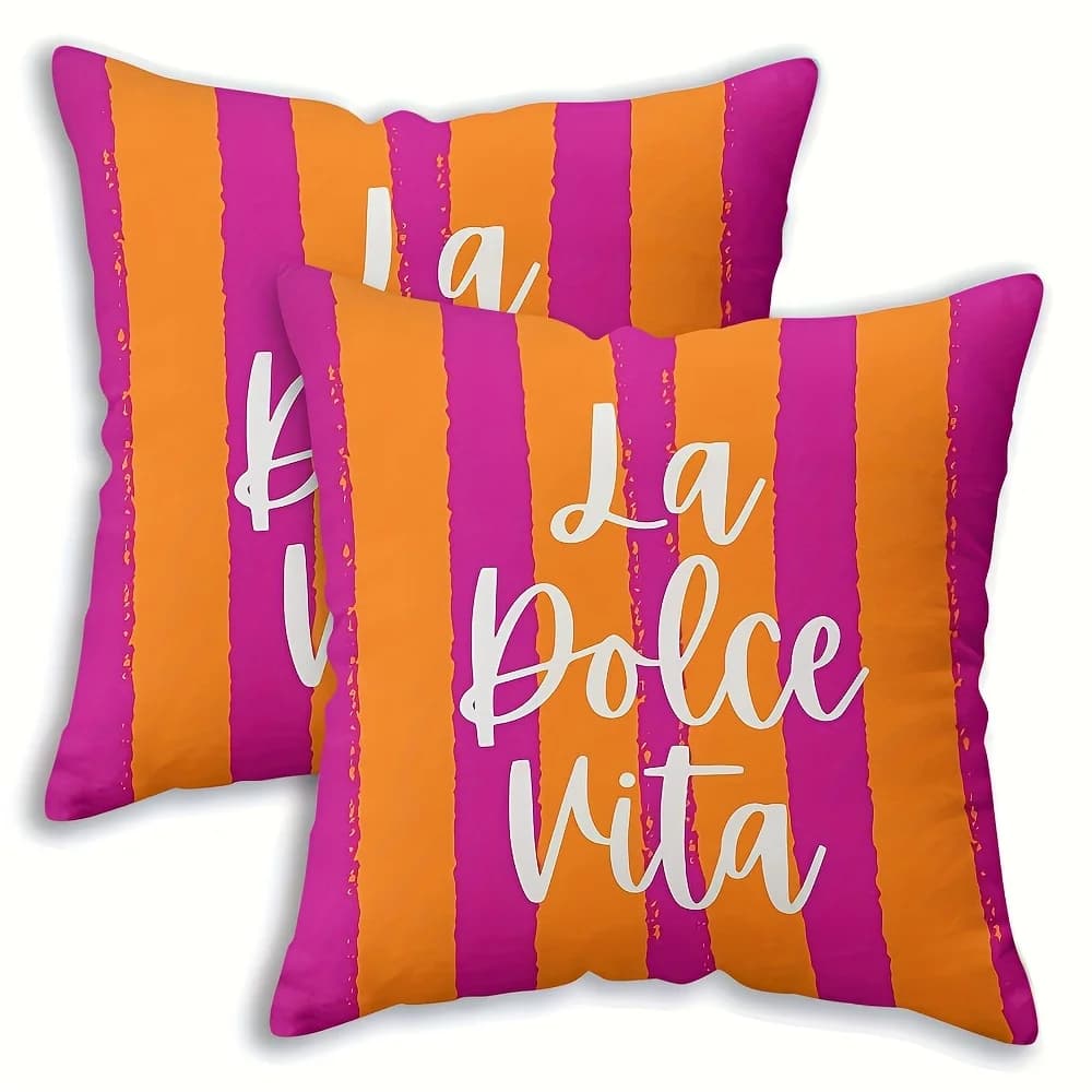 Duas almofadas decorativas listradas roxo e laranja com texto 'La Dolce Vita' sobre sofá.
