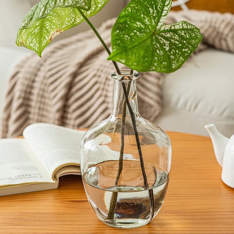 Vaso para plantas Jácotei em vidro transparente com arranjo floral verde sobre mesa de madeira