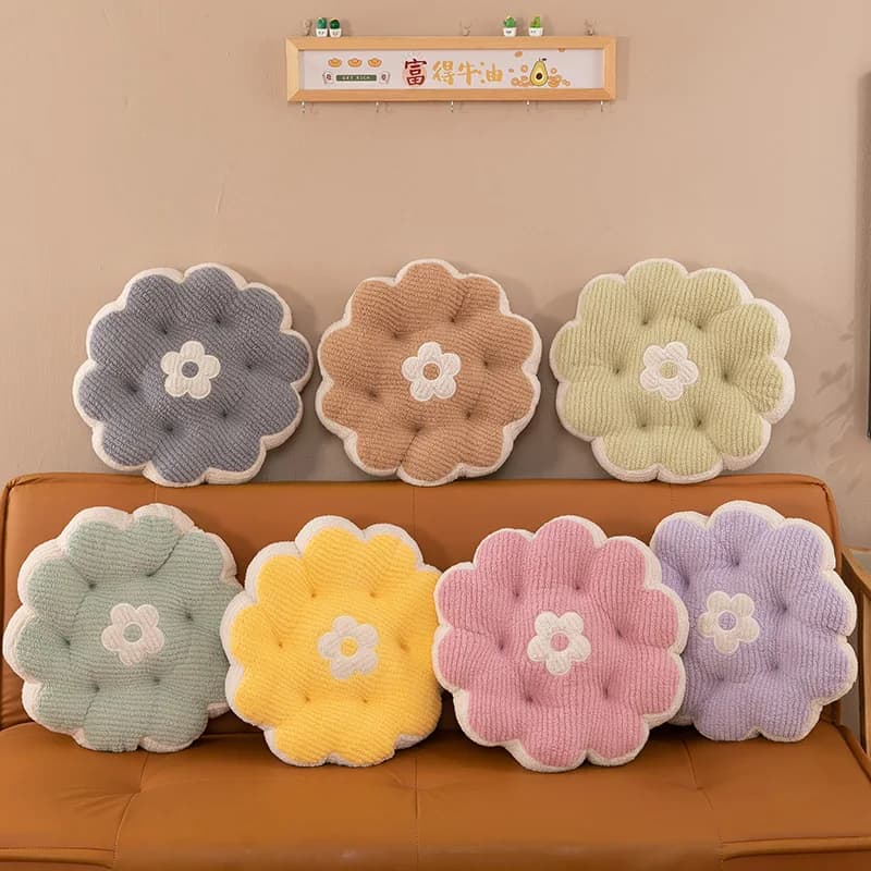 Sete almofadas decorativas de pelúcia em forma de flor, cores pastel, sobre um sofá marrom