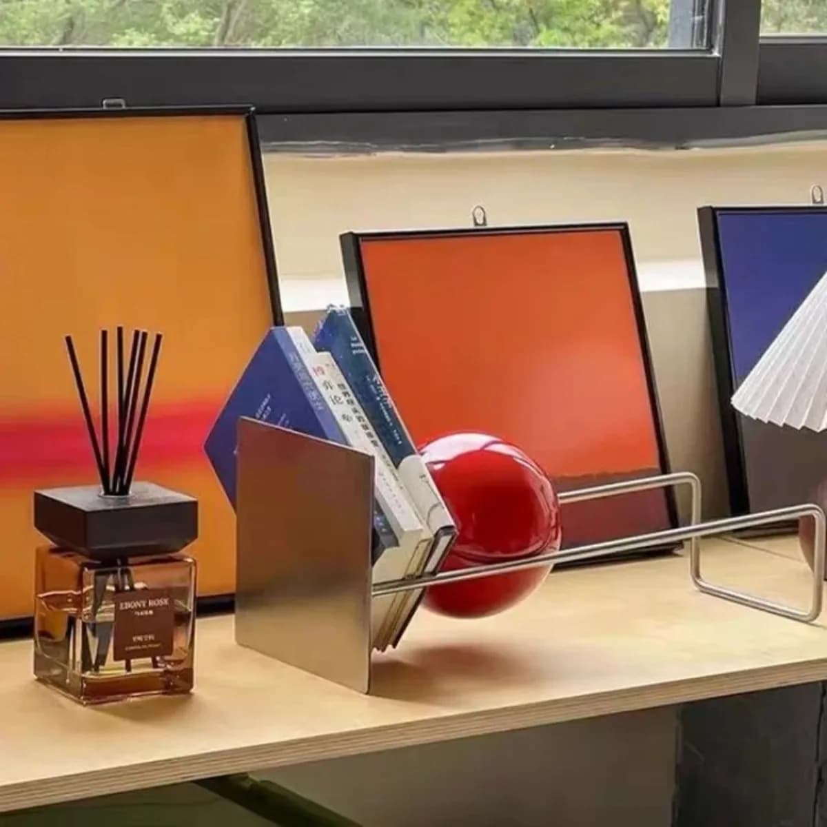 Estante de livros em aço inoxidável criativa para mesa, com livros e uma bola vermelha.