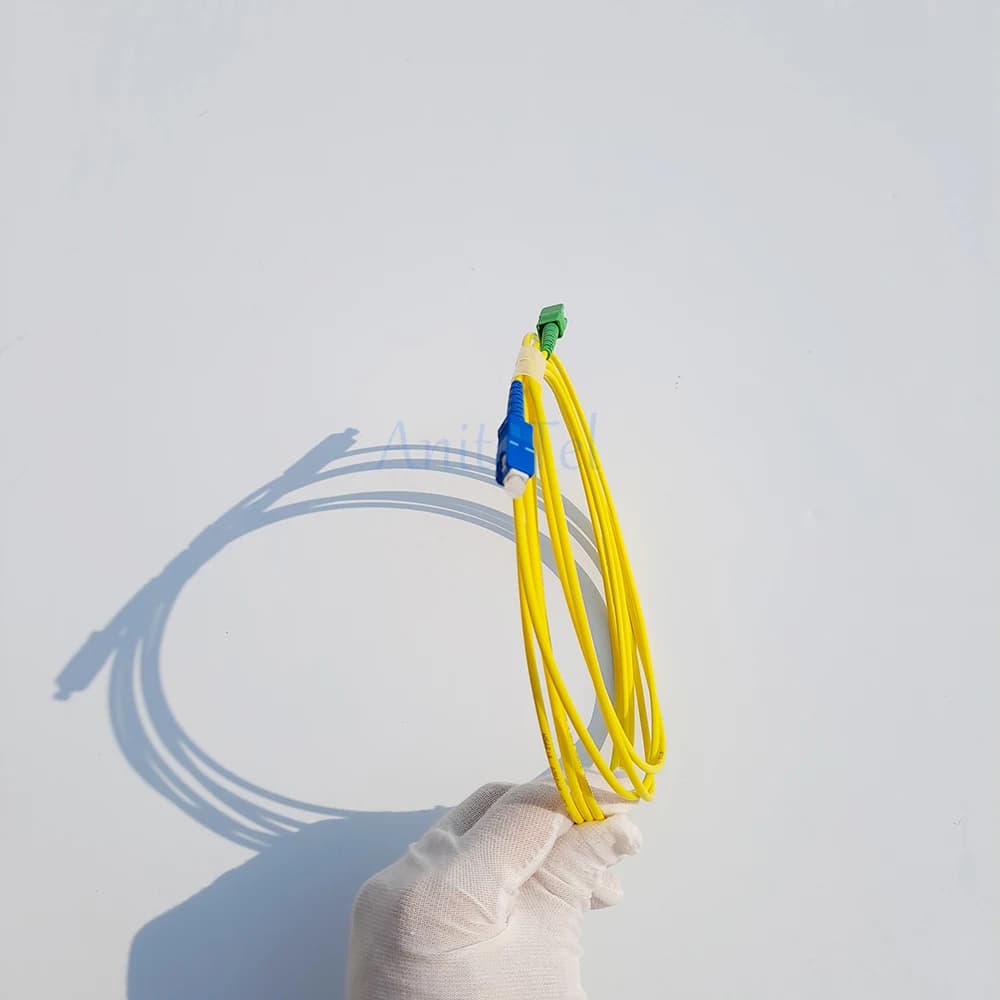 Mão com luva segurando cabo de remendo fibra óptica monomodo amarelo com conectores SC/APC verde e SC/UPC azul