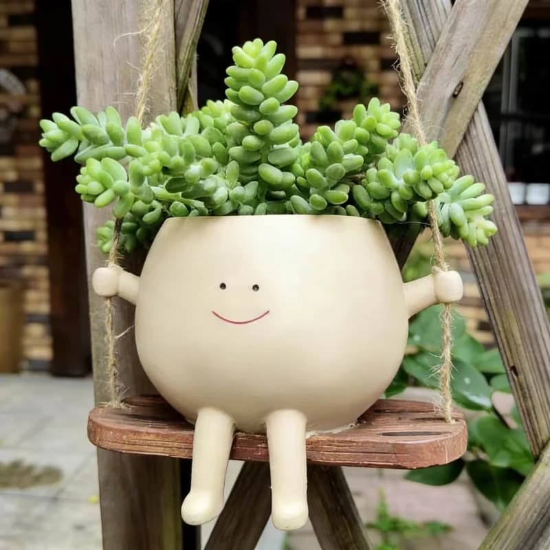 Vaso decorativo bege em resina com rosto sorridente pendurado em balanço de corda com suculenta verde