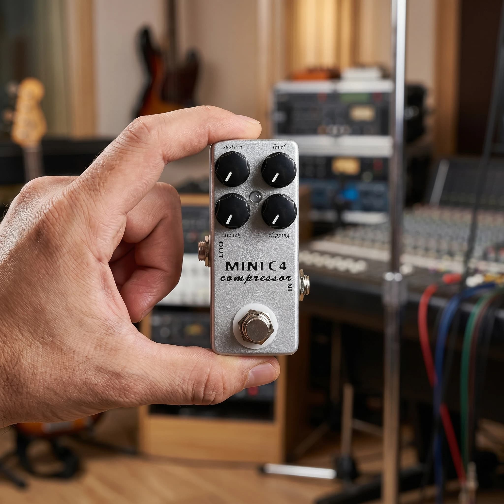 Pedal compressor Mosky MINI C4 cinza sendo segurado com mão em estúdio de gravação musical