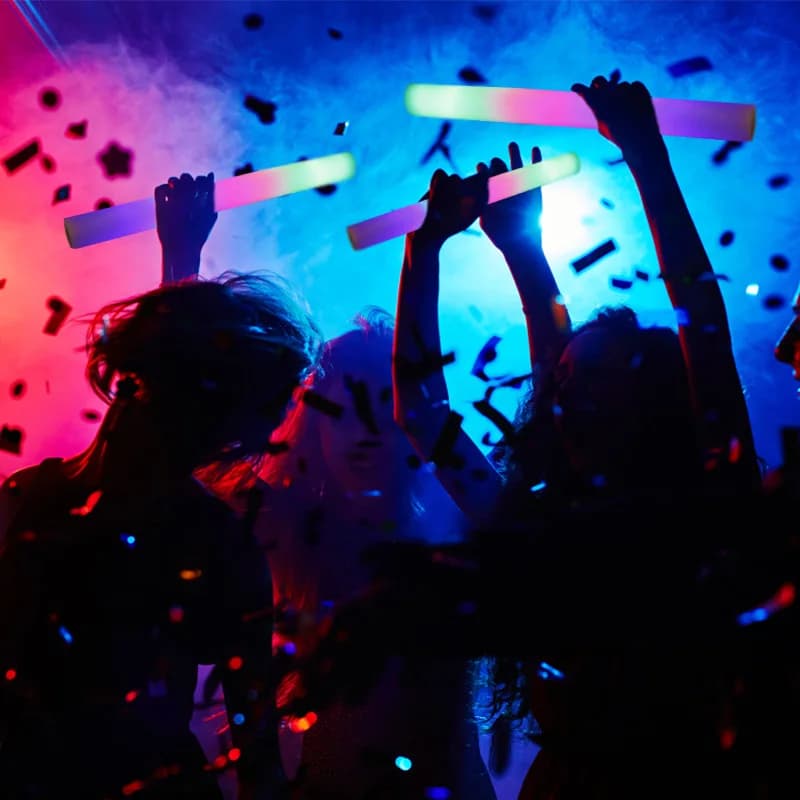 Pessoas segurando varas de LED multicoloridas Jácotei brilho RGB em festa com confetes e iluminação vibrante
