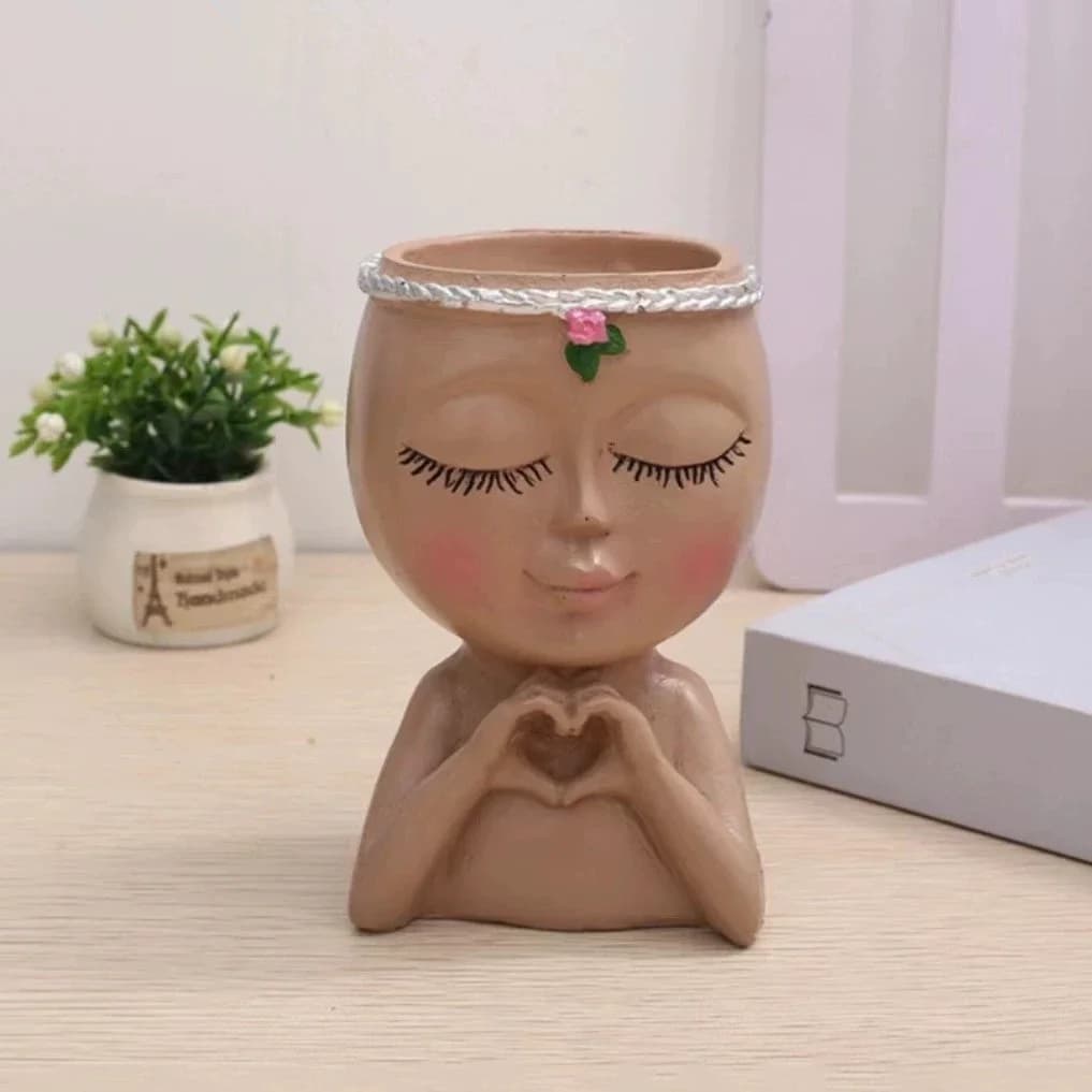 Vaso de resina marrom claro cabeça de senhora mini decorativo sem planta em mesa clara com livro ao lado