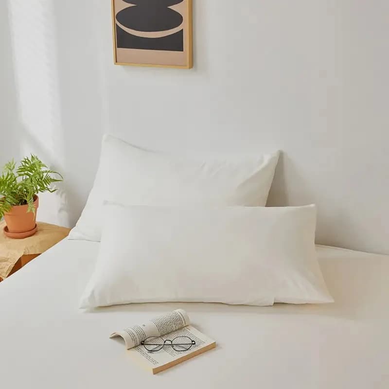 Fronha escovada macia branca em cama com livro aberto e óculos sobre lençol branco