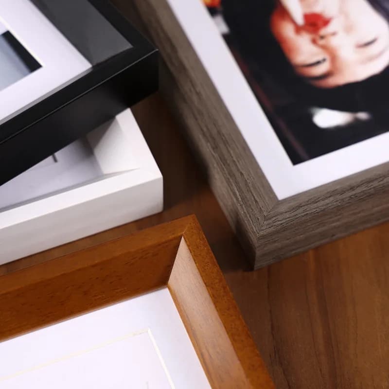 Conjunto de porta-retratos minimalistas em preto, branco, madeira clara e cinza sobre mesa de madeira