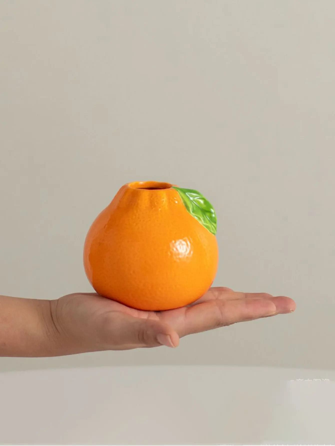 Vaso hidropônico formato laranja segurado na mão, cerâmica laranja com folha verde brilhante