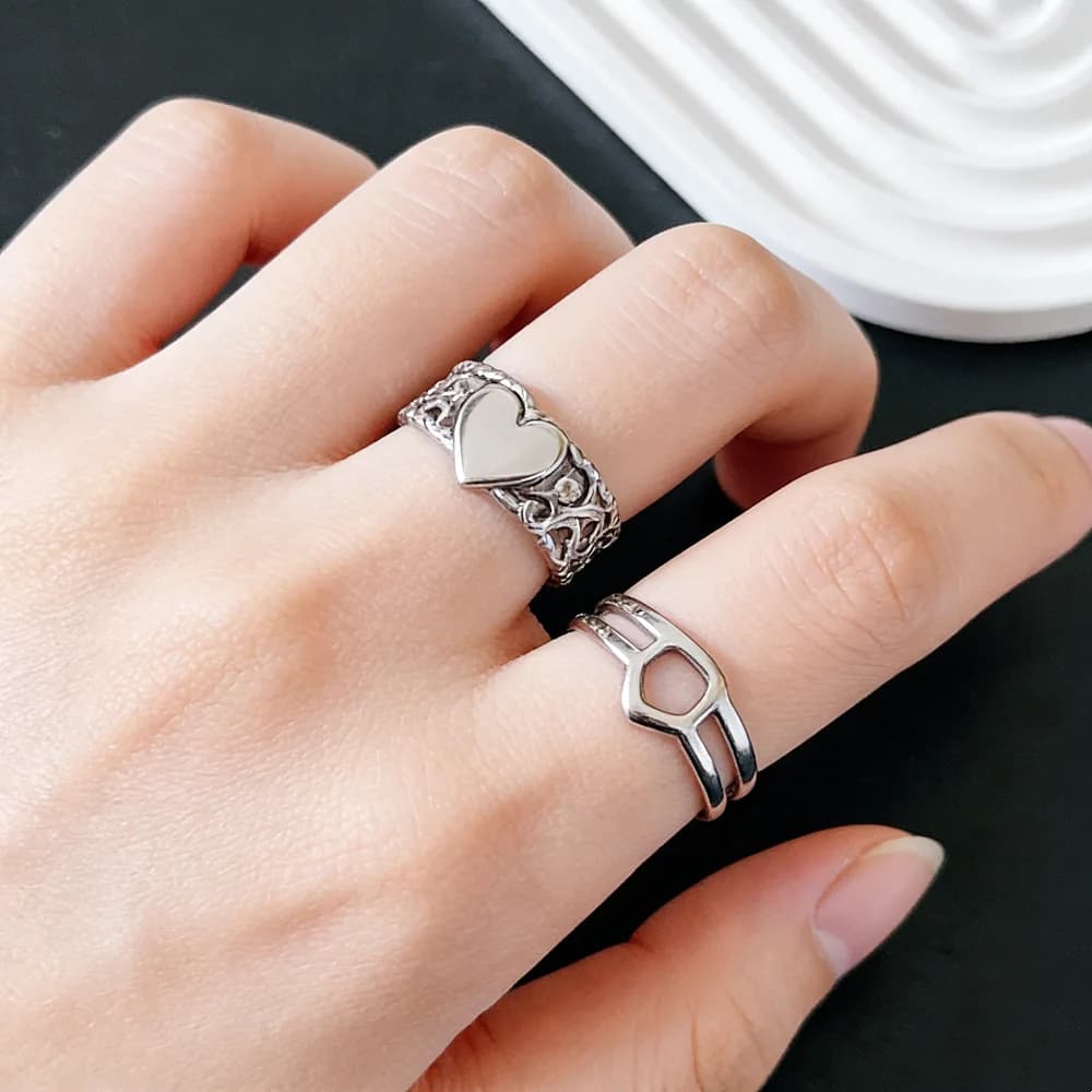 Mão feminina usando dois anéis abertos prateados em aço inoxidável com design delicado