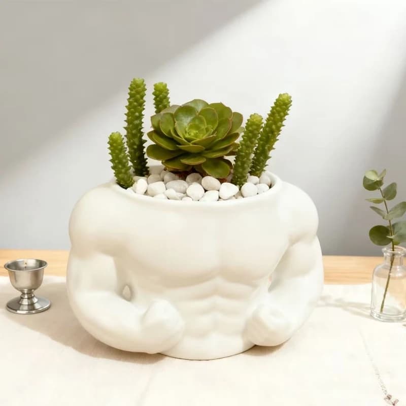 Vaso decorativo em forma de homem musculoso com plantas verdes e cactos, em um suporte de madeira com folhas de ginkgo.