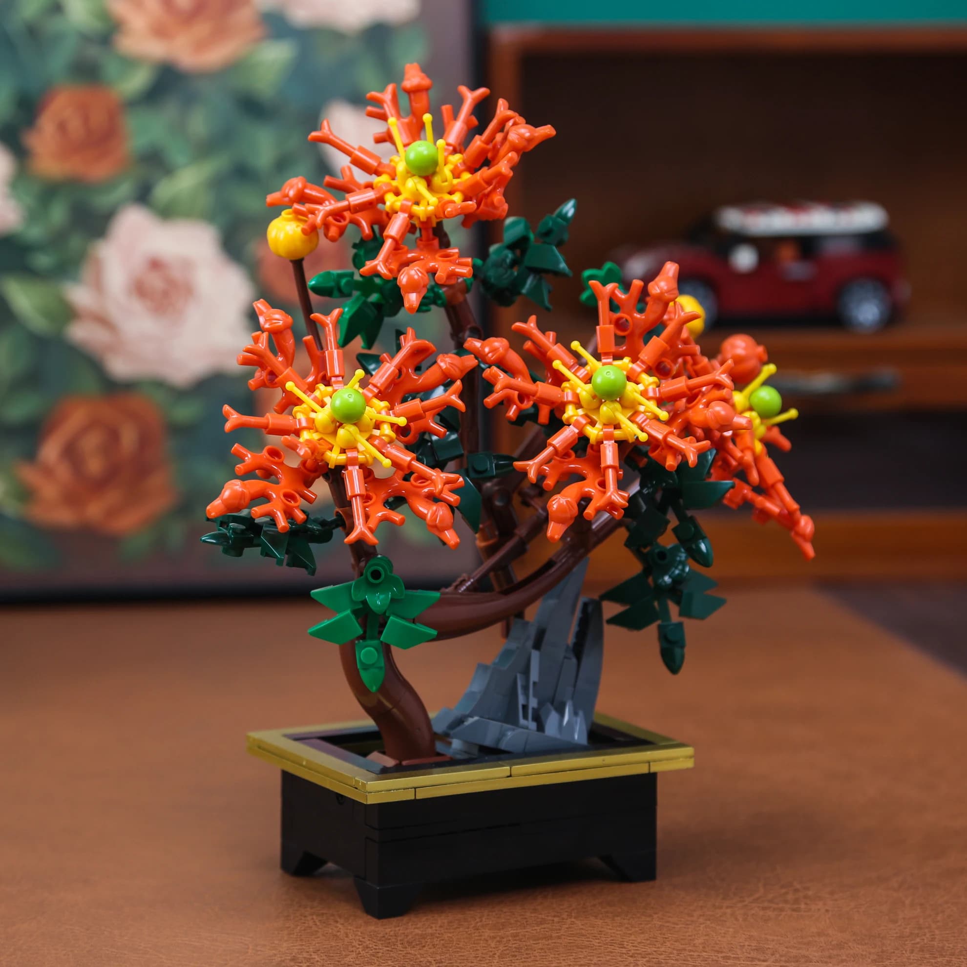Bonsai de montar DIY com flores laranja e folhas verdes em vaso preto com detalhes dourados