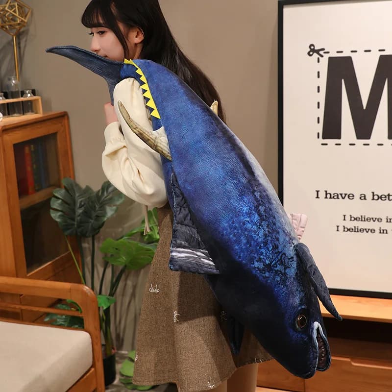 Almofada macia de pelúcia atum azul com detalhes amarelo e branco sendo carregada no ombro