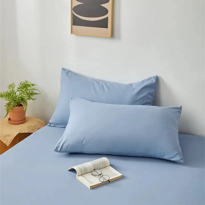 Fronha escovada macia azul em cama com livro aberto e óculos sobre lençol azul