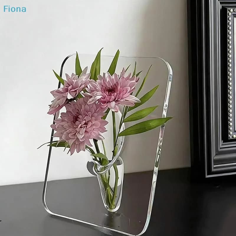 Vaso de acrílico transparente com flores púrpuras e verdes, sobre um livro, com reflexo em espelho.