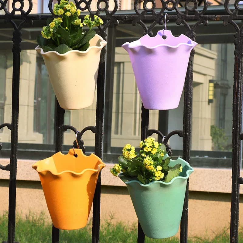 Vasos de flores Jácotei em plástico colorido com flores amarelas pendurados em grade metálica