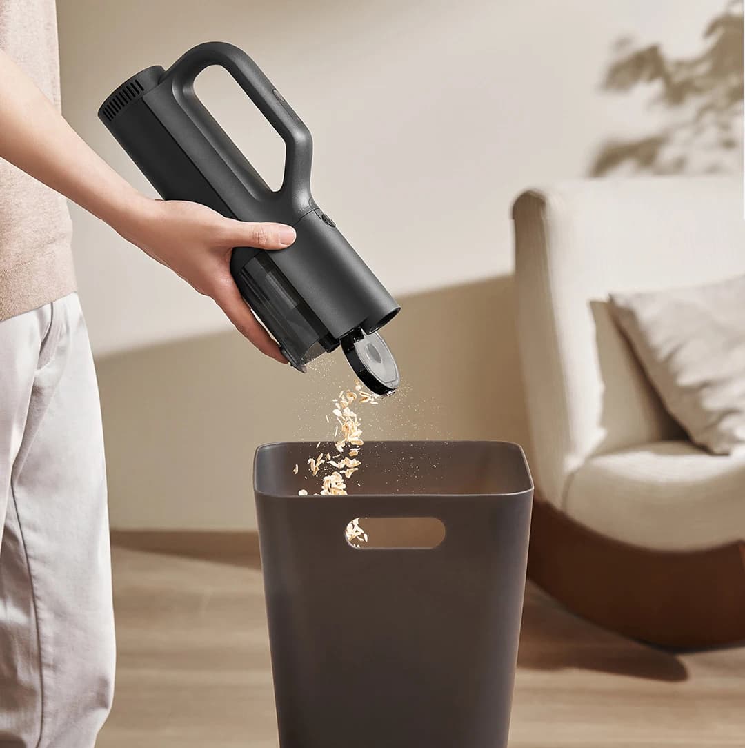 Aspirador de pó portátil MIJIA preto sendo esvaziado em lixeira, design sem fio compacto