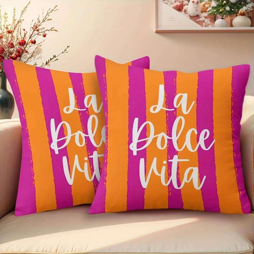 Duas almofadas decorativas listradas roxo e laranja com texto 'La Dolce Vita' sobre sofá.