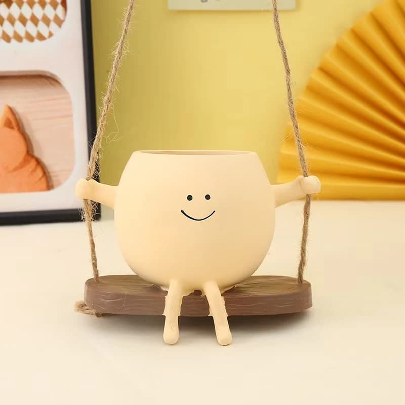 Vaso decorativo bege em resina com rosto sorridente pendurado em balanço de corda para plantas