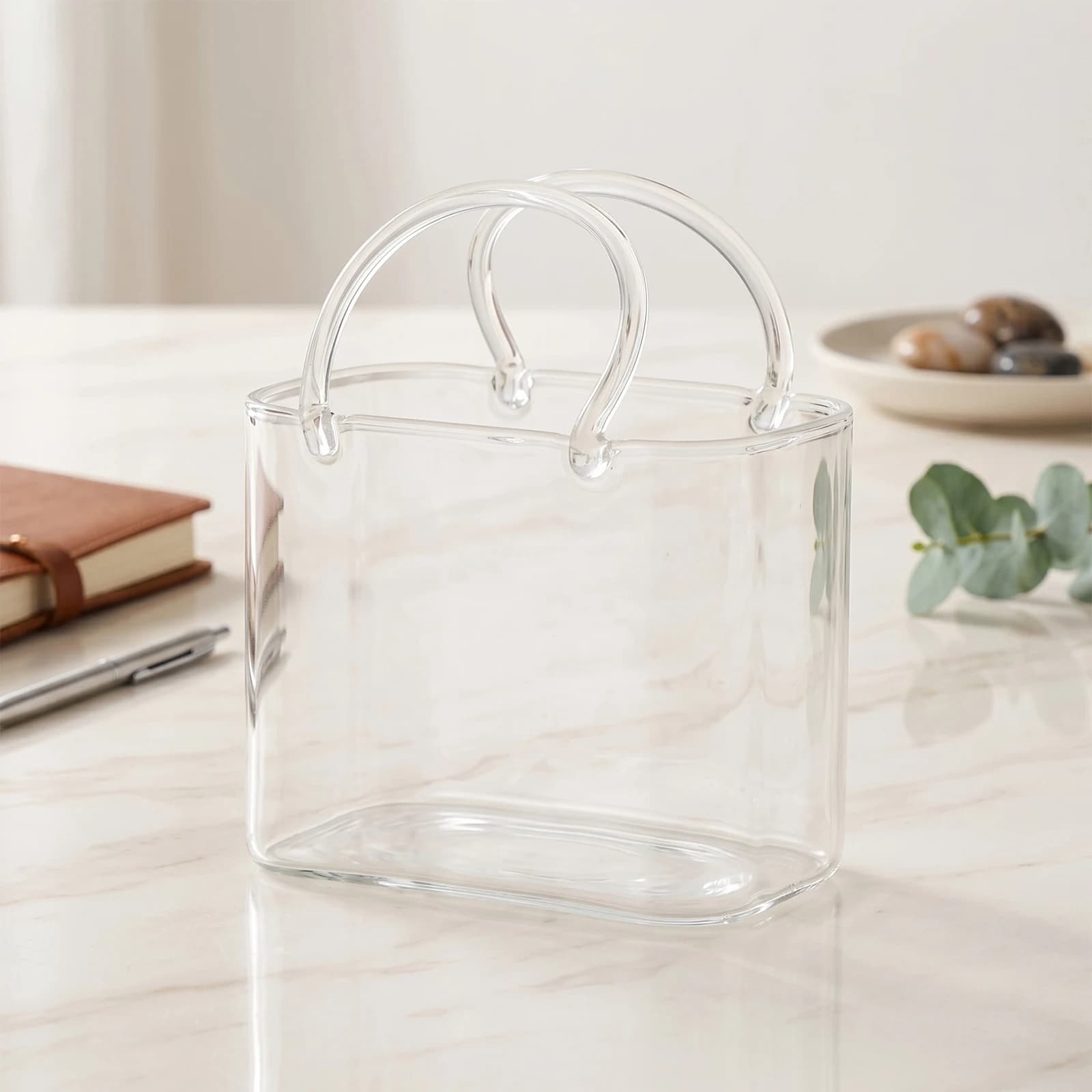 Copo de vidro transparente formato bolsa vazio em bancada clara com decoração minimalista ao fundo