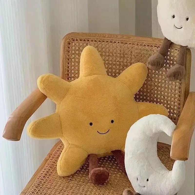 Almofada de pelúcia amarela em forma de sol com rosto sorridente e almofada de lua branca com rosto feliz