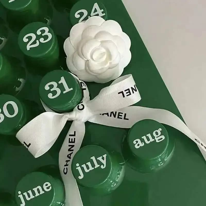 Detalhe de calendário perpétuo verde com laço branco Chanel e flor decorativa branca