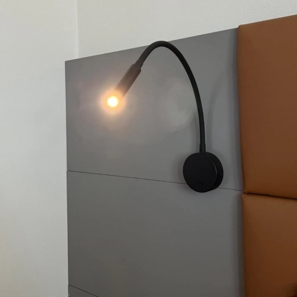 Arandela de parede Tokili Gooseneck preta com braço flexível e LED aceso instalada em cabeceira cinza