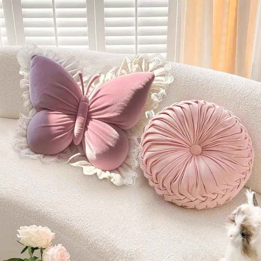 Almofada borboleta rosa em veludo com renda ao lado de almofada redonda rosa em sofá branco