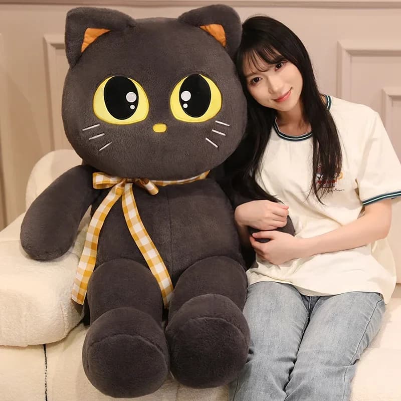 Almofada de pelúcia gato kawaii macia 60cm cinza com laço xadrez amarelo ao lado de mulher sentada
