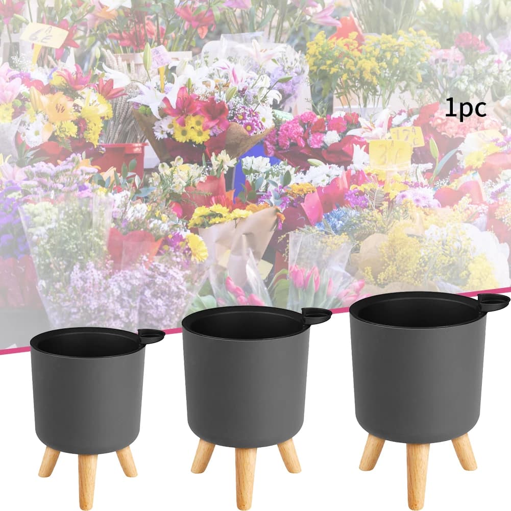Vasos de plantas artificiais com base redonda branca e pernas de madeira em um ambiente interno.