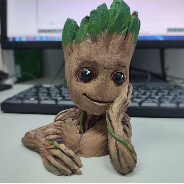 Miniatura de Groot, personagem dos Guardiões da Galáxia, em pé, com detalhes pintados à mão, em um fundo de mesa de escritório.