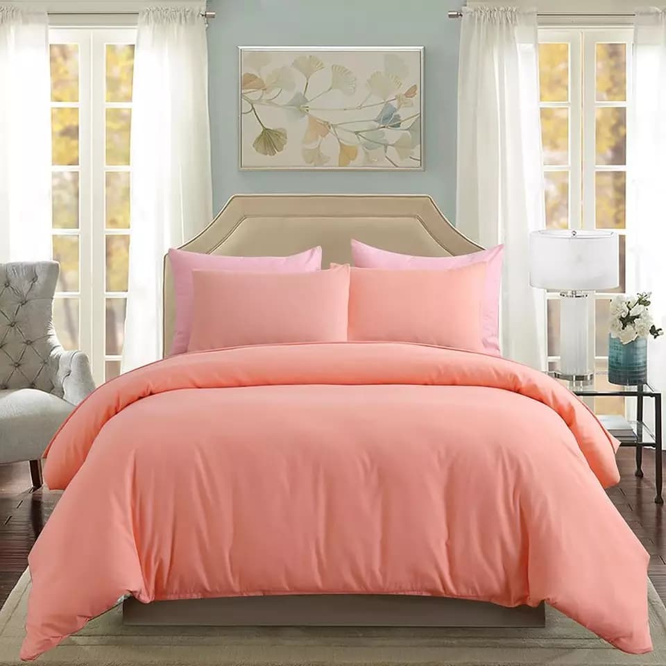 Edredom rosa claro de algodão com almofadas combinando, conjunto de cama confortável em um quarto neutro.
