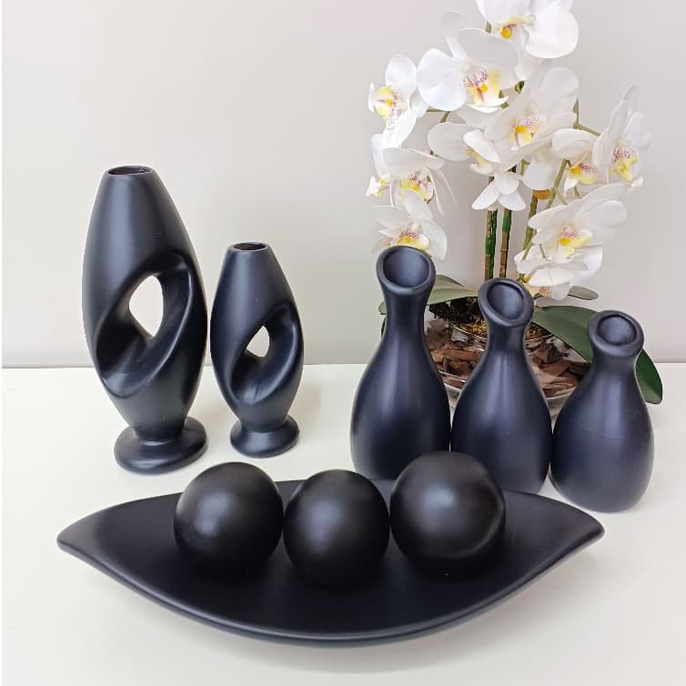 Conjunto decorativo de nove peças de cerâmica preta com três vasos grandes, três menores e três esferas pretas em uma placa, com flores brancas no fundo