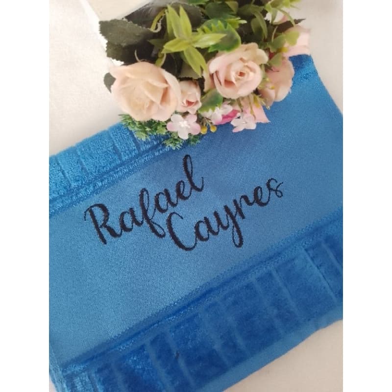 Toalha azul bordada com o nome Rafael Cayres e buquê de flores rosas