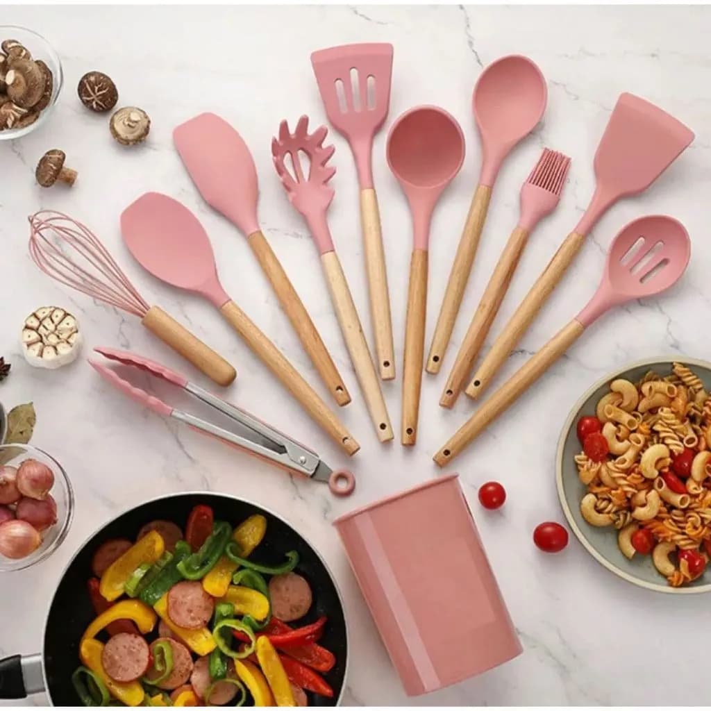 Conjunto de utensílios de cozinha rosa com cabos de madeira, dispostos sobre uma superfície de mármore branco.