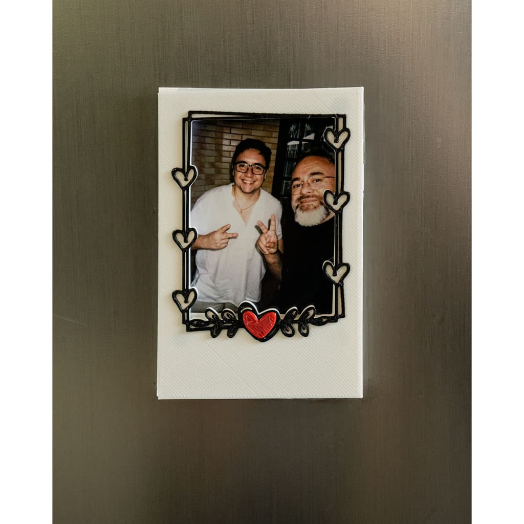 Porta retrato magnético branco com moldura preta e coração vermelho, foto de dois homens sorrindo