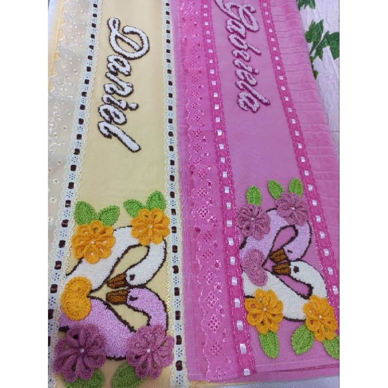 Toalha de banho personalizada com bordado de cisnes e flores, nomes Débora e Gabriela, fundo rosa e amarelo.