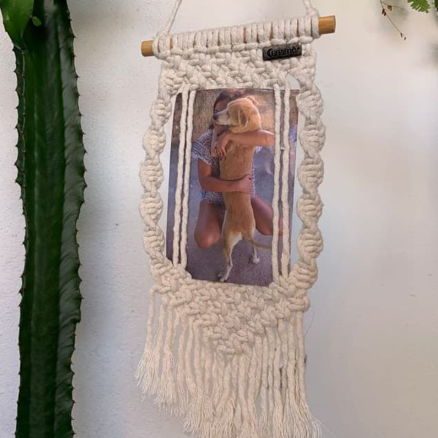 Porta-retrato artesanal com macramê branco, moldura e foto de uma mulher abraçando um cachorro