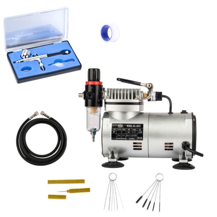 Compressor para aerógrafos com kit de limpeza, fundo branco, compressor prateado e preto, kit de ferramentas e agulhas.