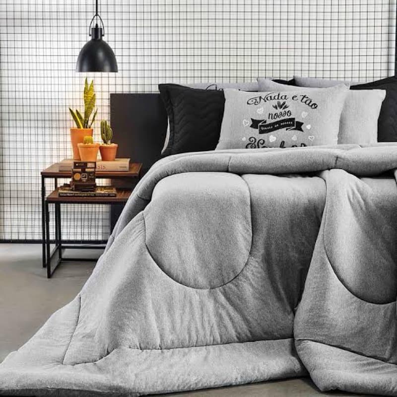 Edredom solteiro cinza com estampa, sobre cama com almofadas pretas e cinza, em quarto com decoração minimalista.
