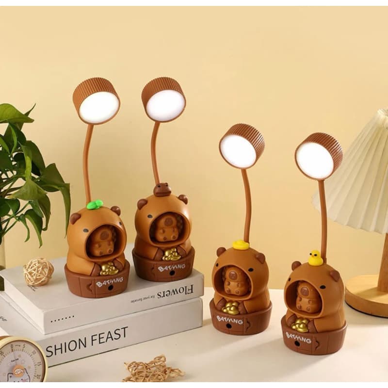 Luminárias de mesa com design de capivara em marrom, iluminadas com LED branco sobre livros.