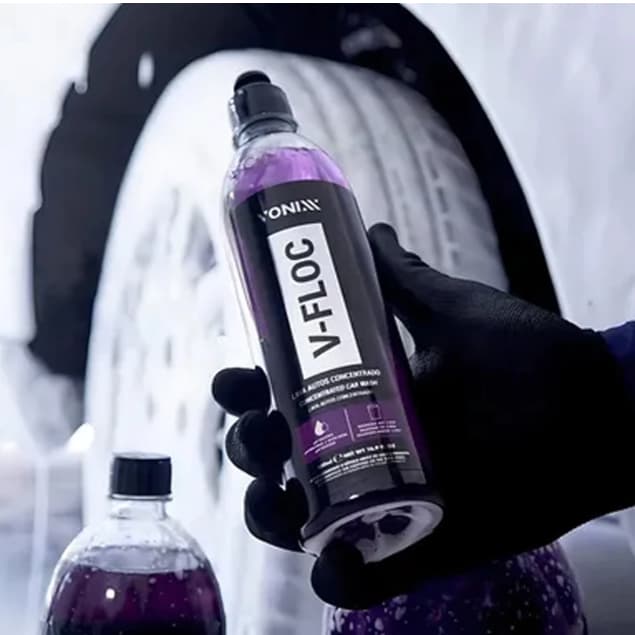 Shampoo automotivo V-Floc da Vonixx, garrafa roxa com rótulo branco e cinza, em mãos com fundo de roda de carro.