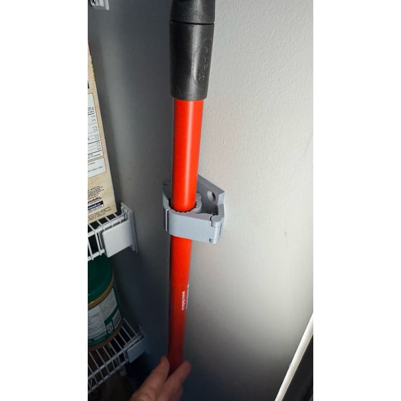 Suporte de vassoura com fita 3M fixado em parede bege com vassoura laranja e preta.