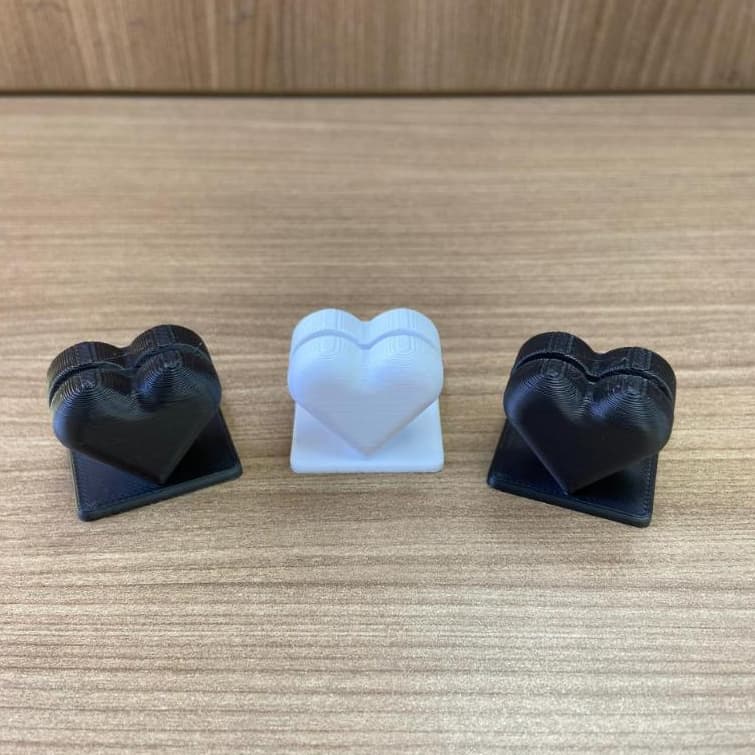 Porta-retratos em forma de coração 3D, branco e preto, sobre fundo de madeira.