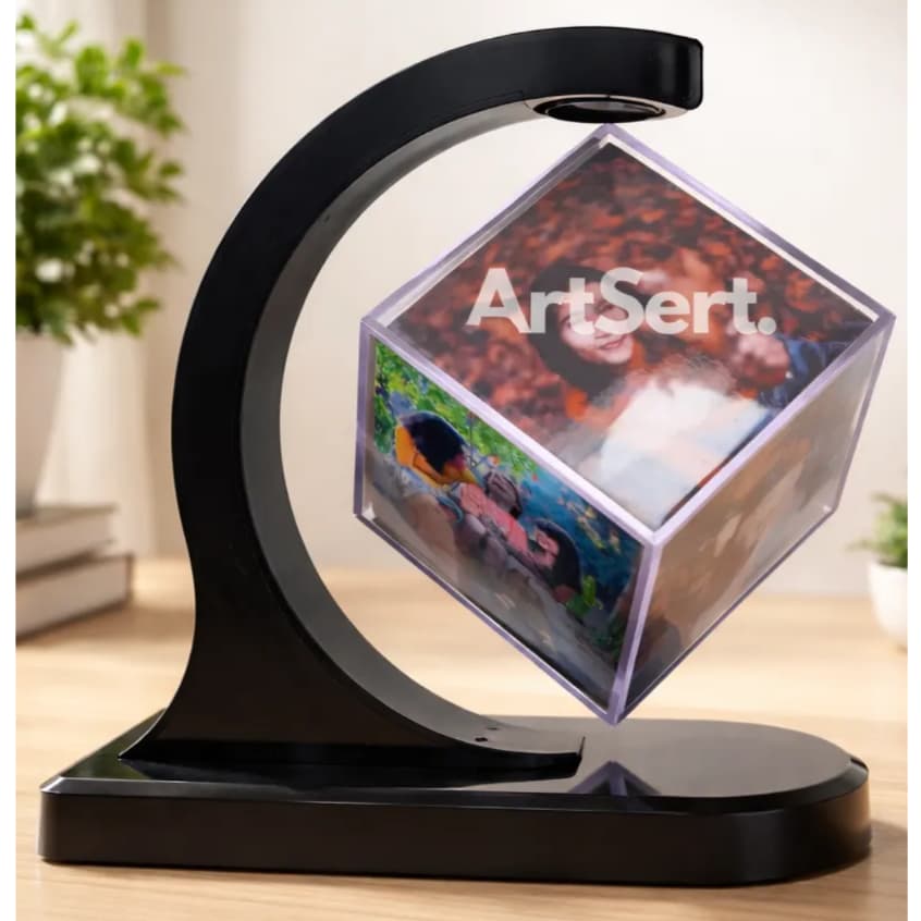 Porta retrato em forma de cubo de fotos magnético personalizado, transparente com bordas pretas, em suporte giratório, com fotos de pessoas, fundo branco, planta verde e livros.