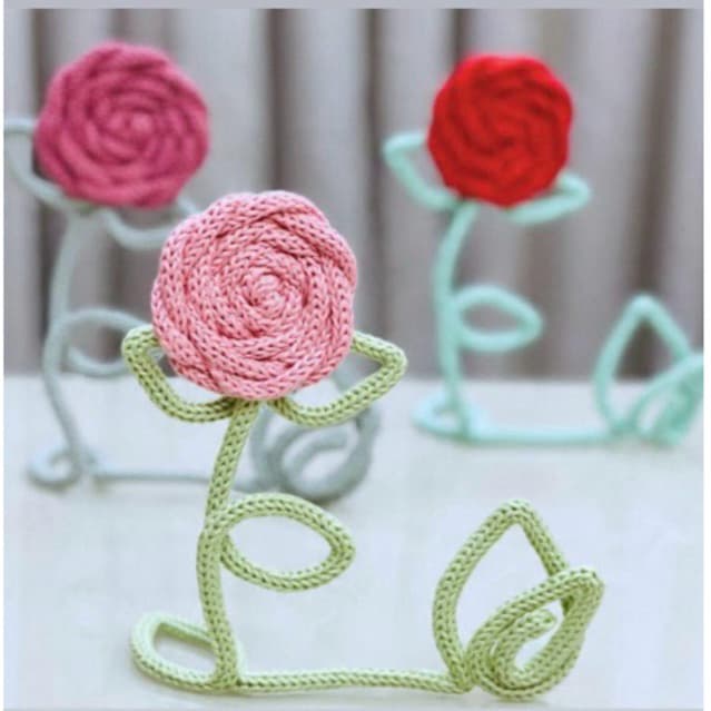 Rosas artesanais em tricotin em cores rosa, vermelha e turquesa sobre fundo acinzentado