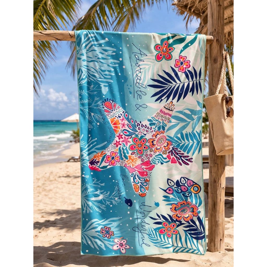 Toalha de praia estampada com estrela e flores, pendurada na areia, fundo azul com texto 'Amor e Liberdade'.